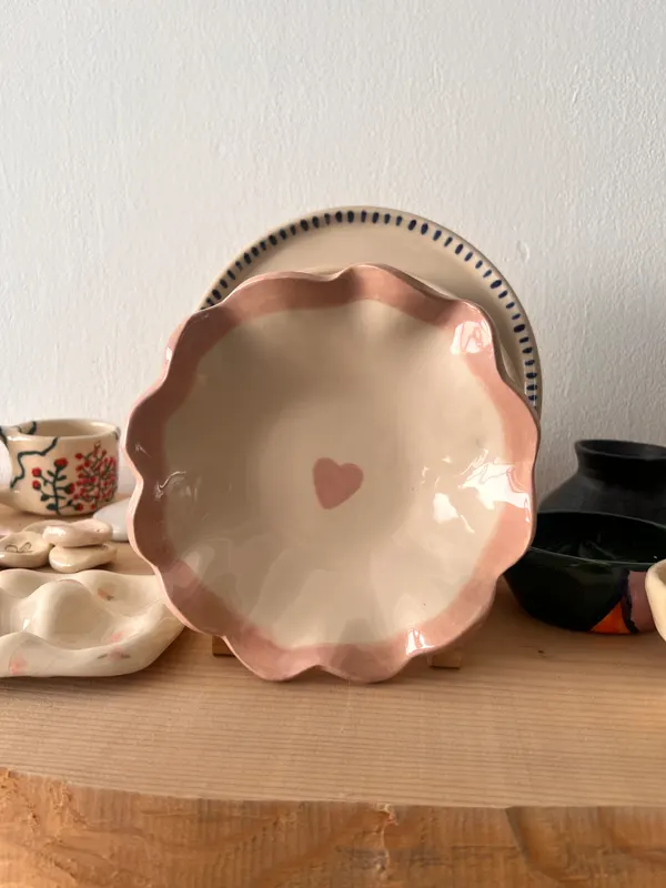 Plato hondo de cerámica de borde ondulado, esmaltado en rosa, con un corazón en el fondo